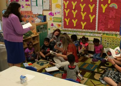 Adults and preschool children read books together during a classroom literacy activity.