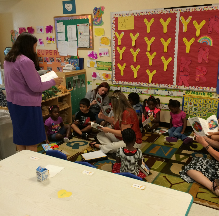 Adults and preschool children read books together during a classroom literacy activity.