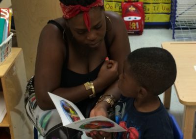 A woman and a young boy look through a children’s book together in a classroom.