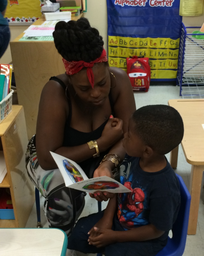 A woman and a young boy look through a children’s book together in a classroom.